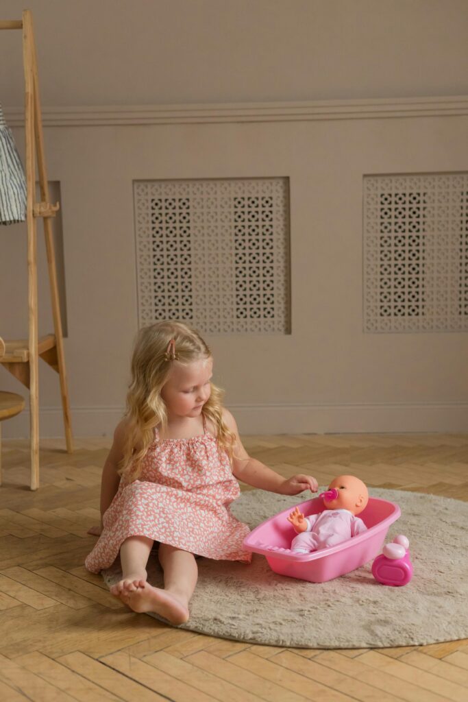 A young girl playing with a baby doll in a pink bathtub, in a warm and cozy indoor setting.