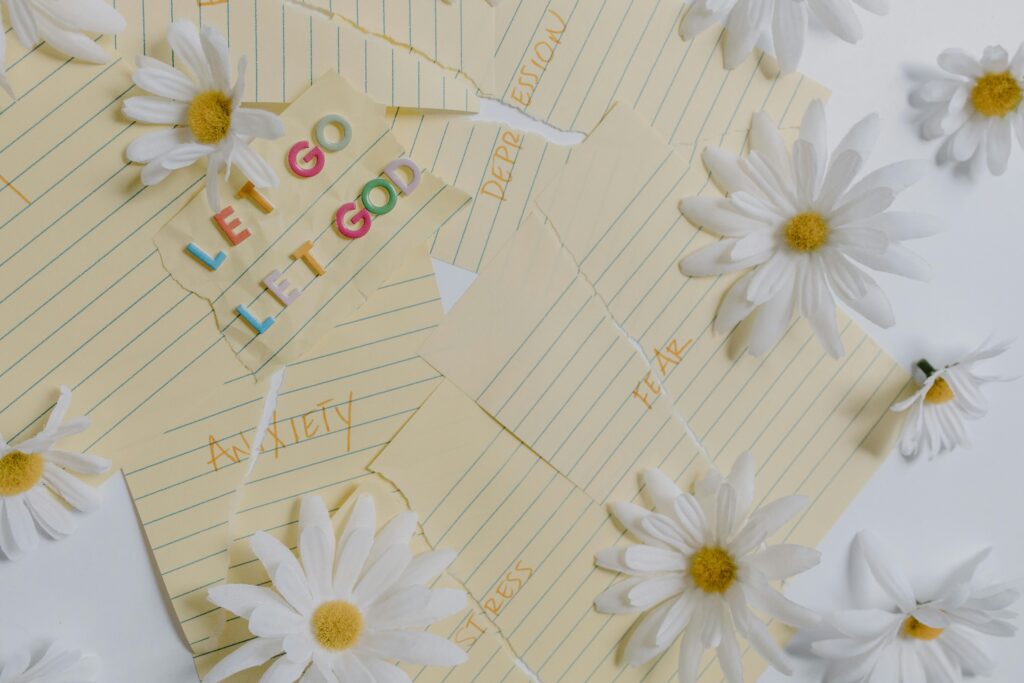 Flat lay of daisies and motivational notes with phrases like 'Let Go Let God' on a white background.
