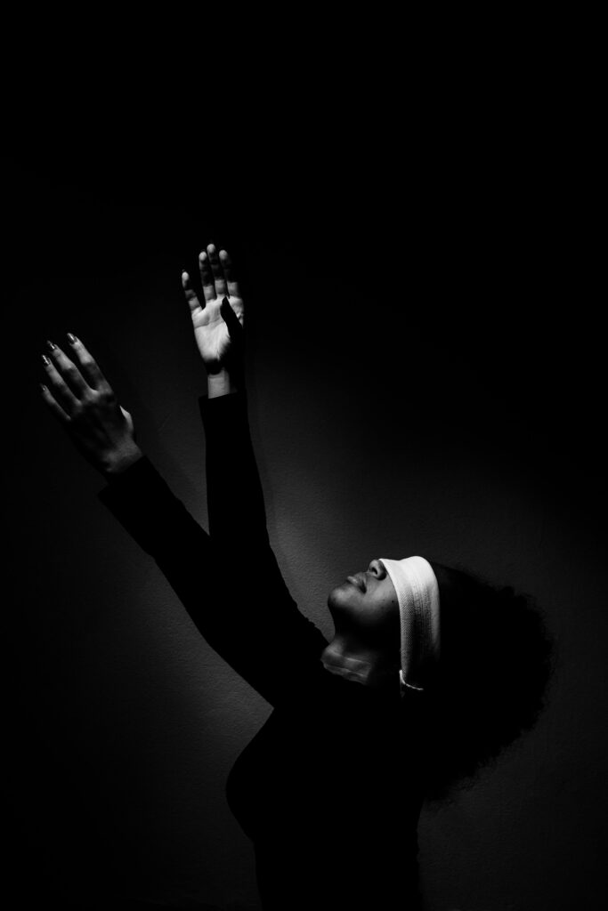Dramatic black and white photo of a blindfolded woman with arms raised.